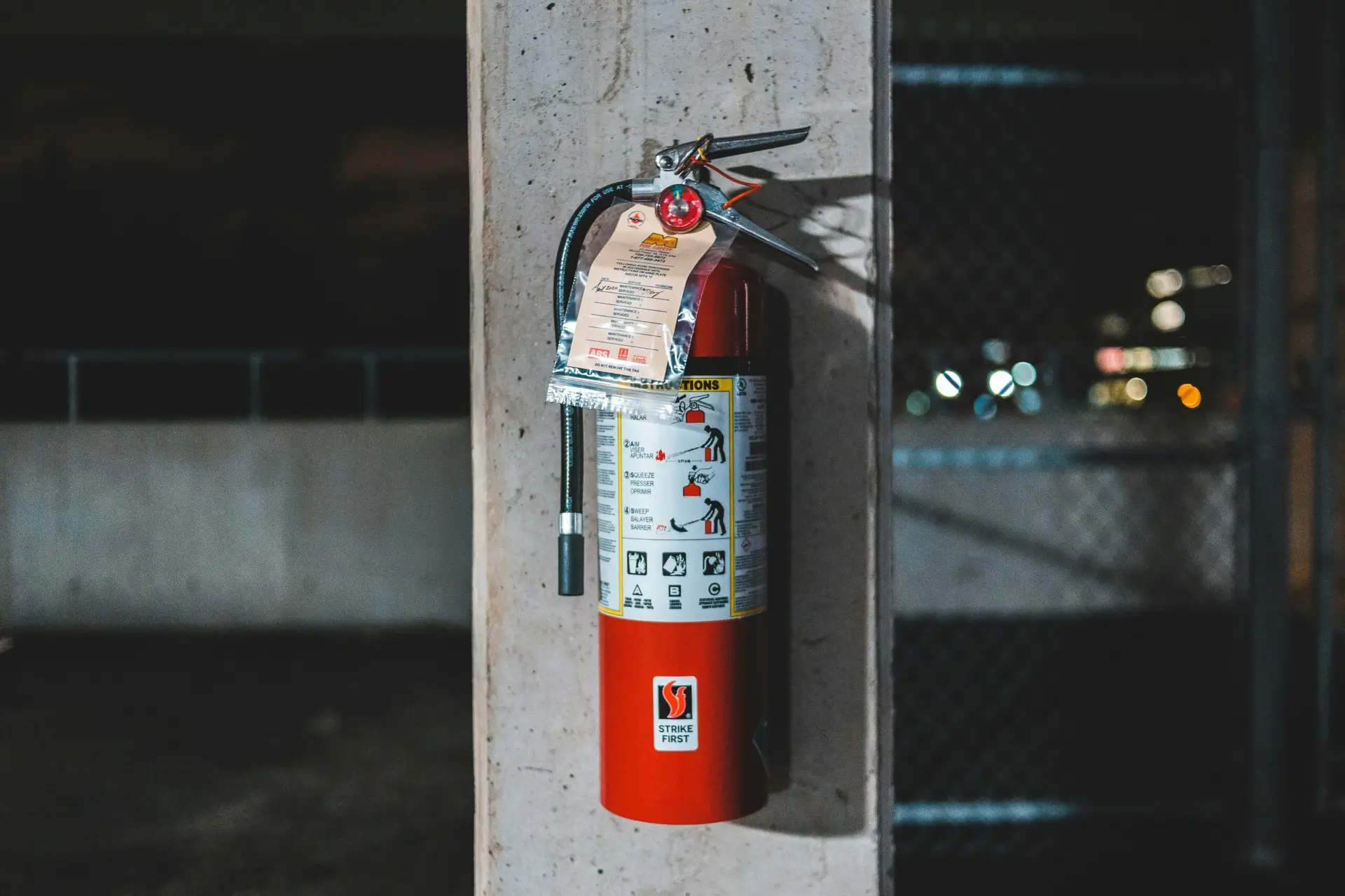 Extinguisher with instruction placed on shabby column near chain link on abandoned industrial zone