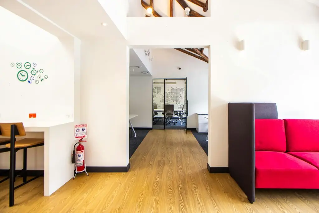 Contemporary office lounge featuring a striking red sofa, wooden floor, and minimal design elements.